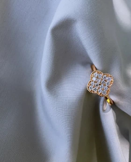 Clover-shaped ring set with clear stones on grey fabric